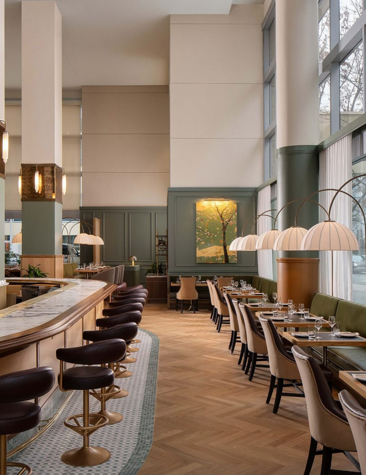 Interior of a modern restaurant with large windows, wooden flooring, and a mix of bar stools and dining chairs around tables.
