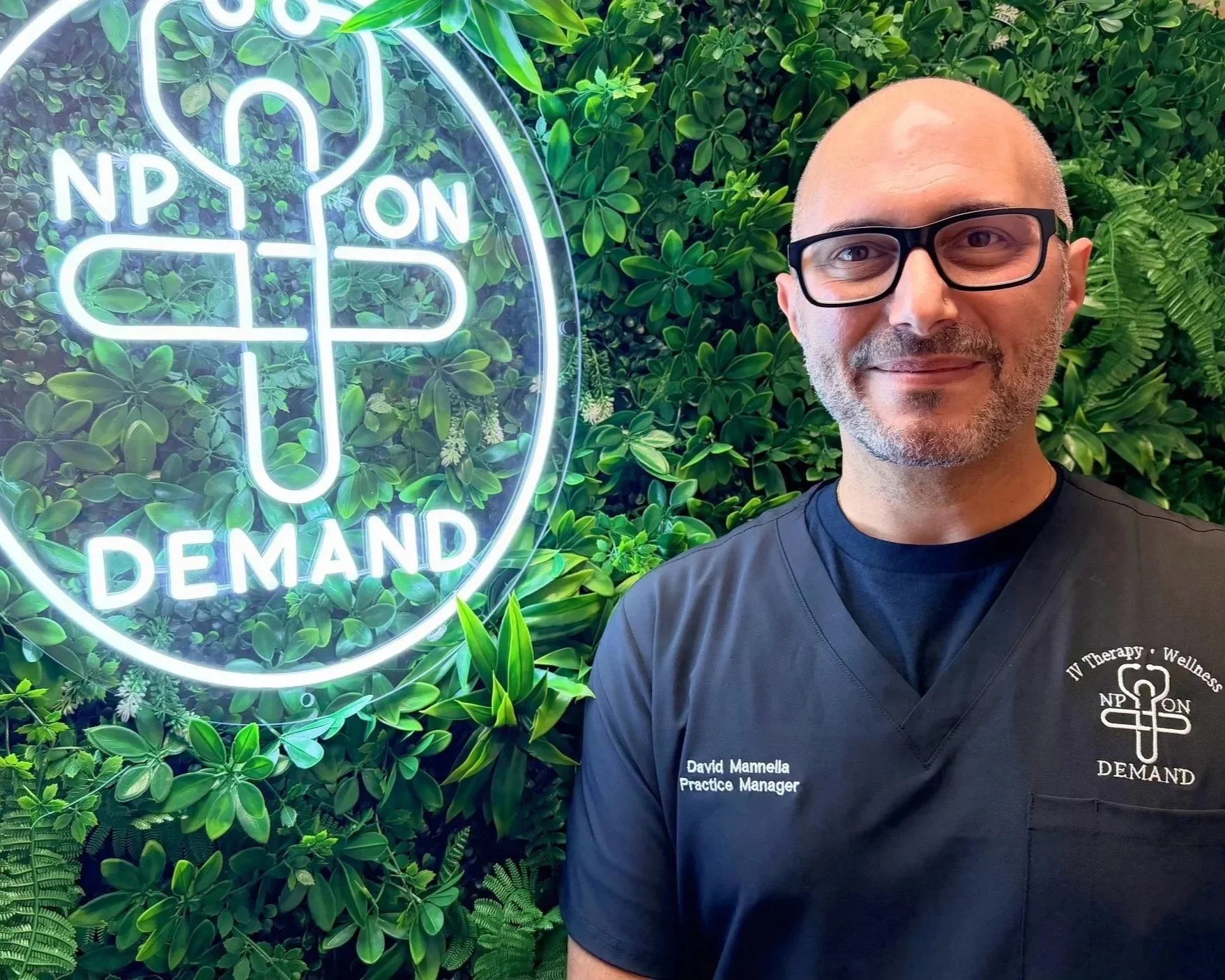 A young man in a gray polo shirt and beige pants sitting on a bench against a beige wall, casting a shadow.