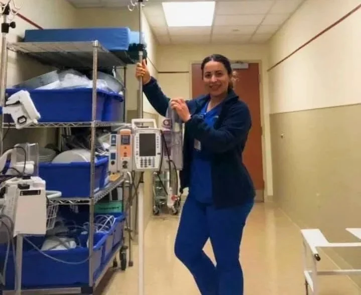A woman sitting on a bench, writing in a notebook, with an abstract painting leaning against the wall beside her.