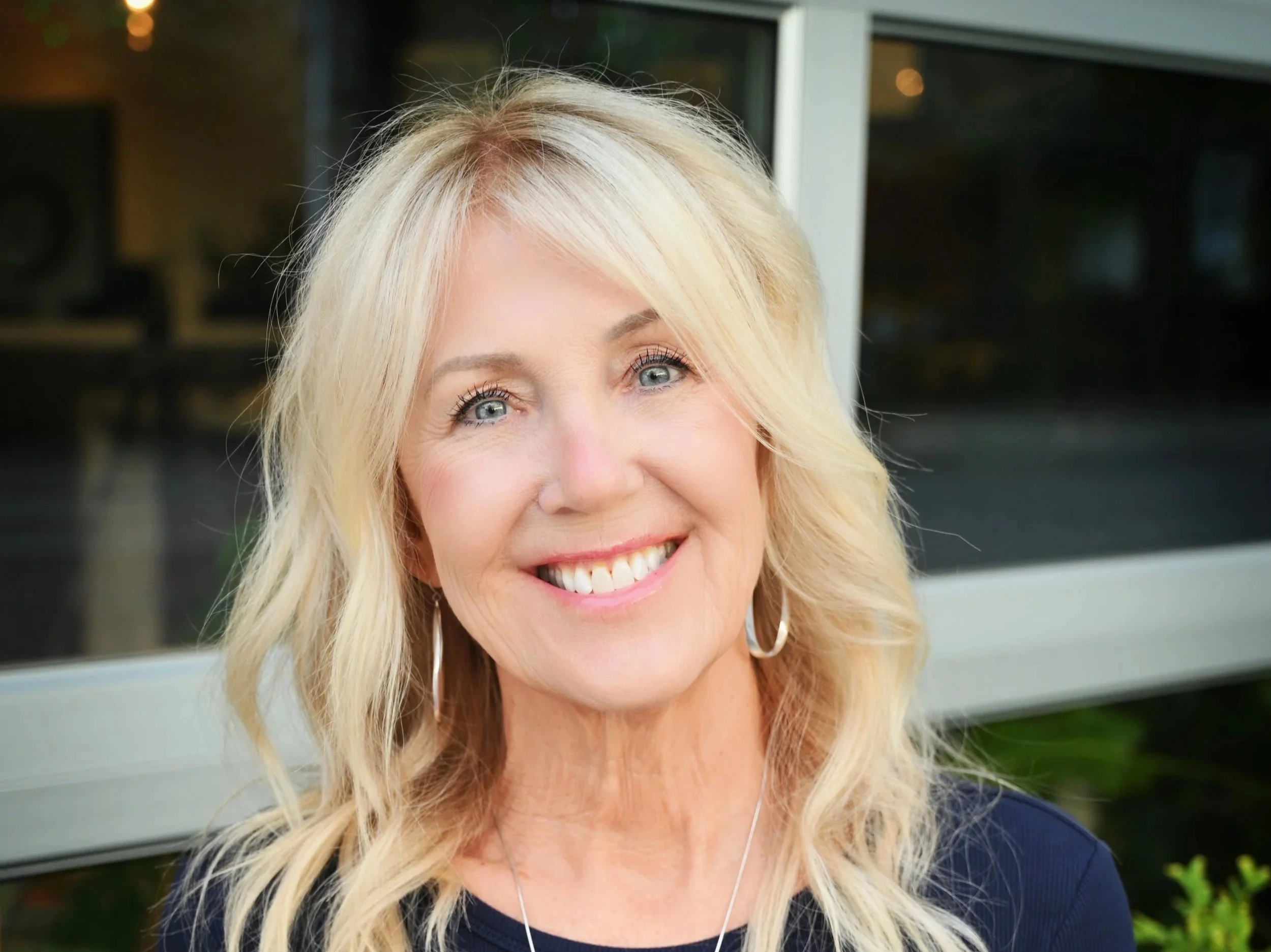A woman with blonde hair and blue eyes smiling outdoors.