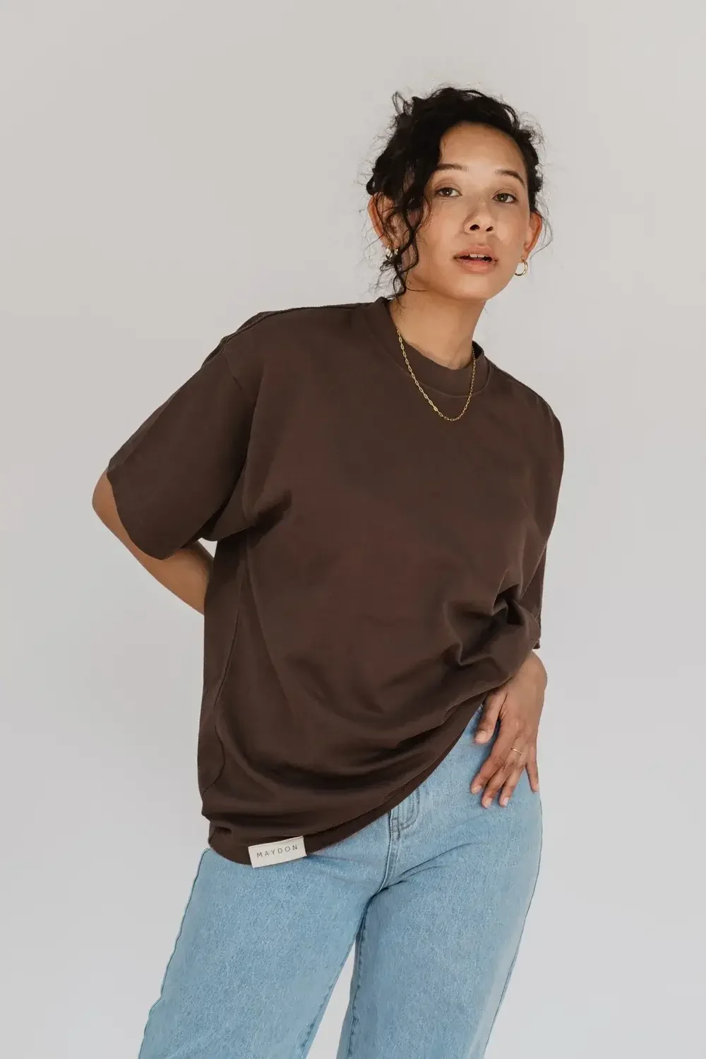 A model wearing a brown t-shirt and jeans stands confidently, showcasing a casual and stylish outfit.