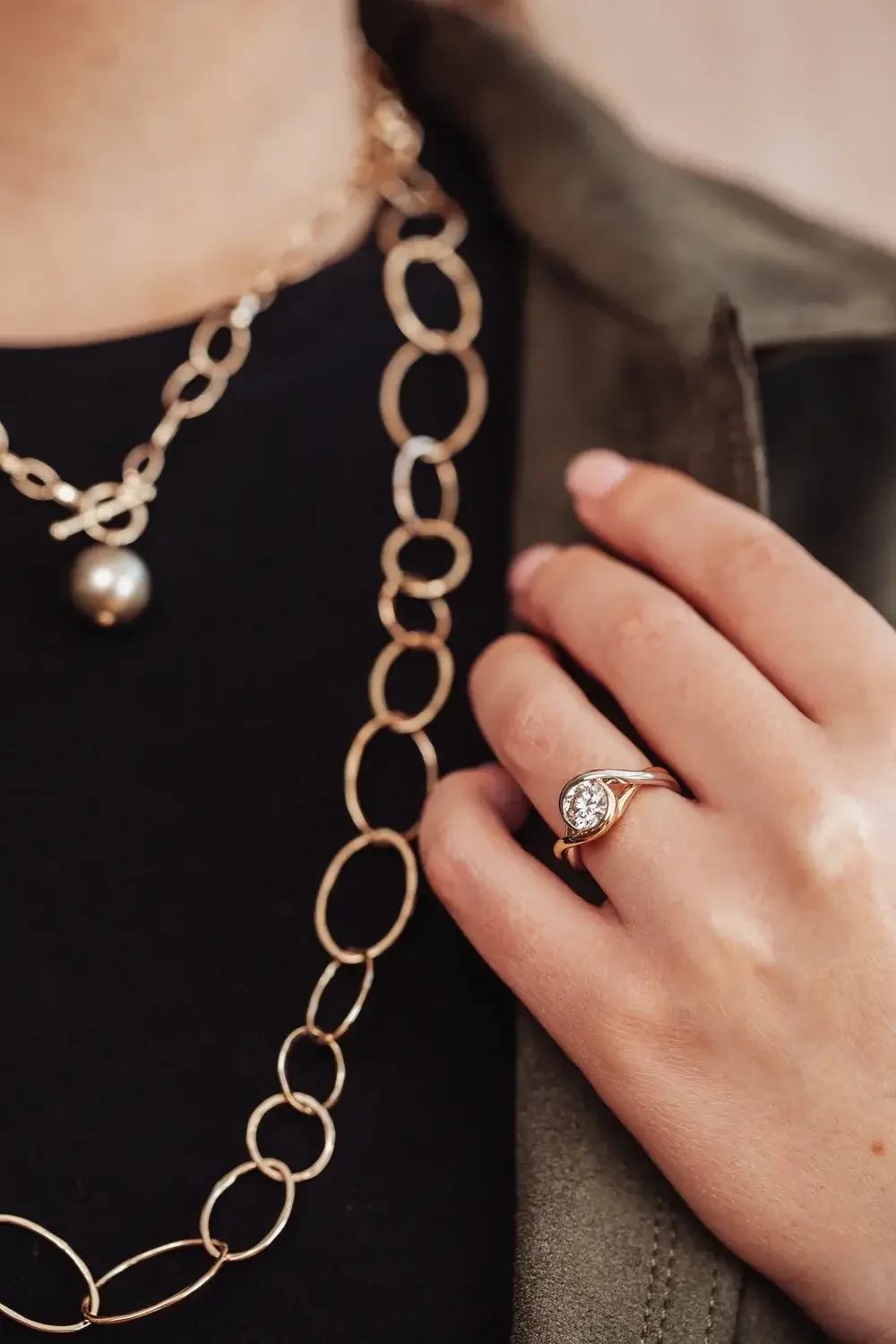 A woman showcases a gold ring on her finger and a matching gold necklace around her neck.
