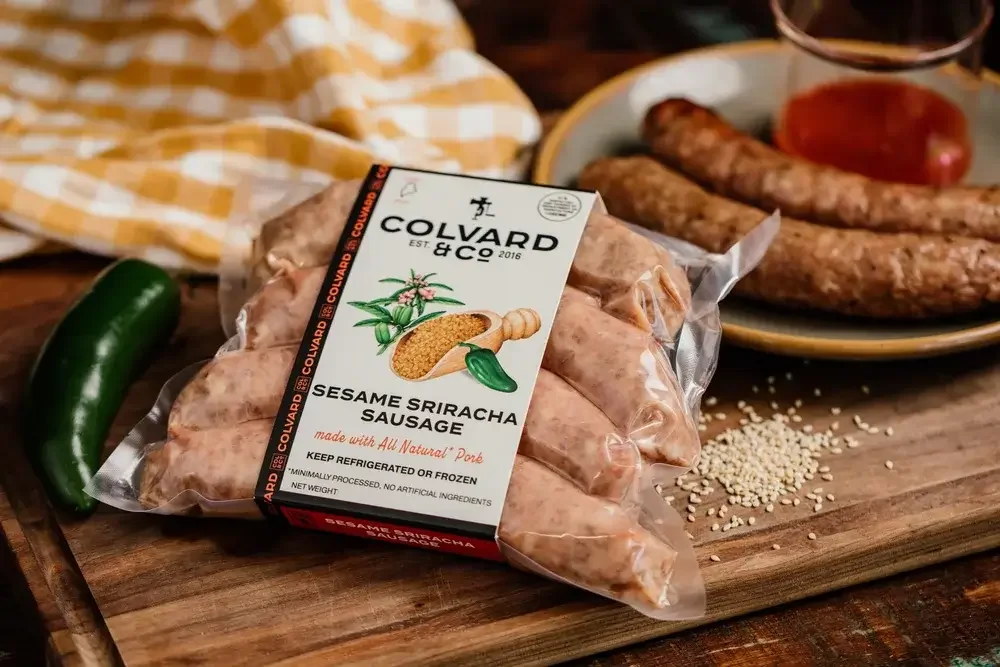 A package of sausages alongside colorful peppers on a wooden cutting board, ready for meal preparation.
