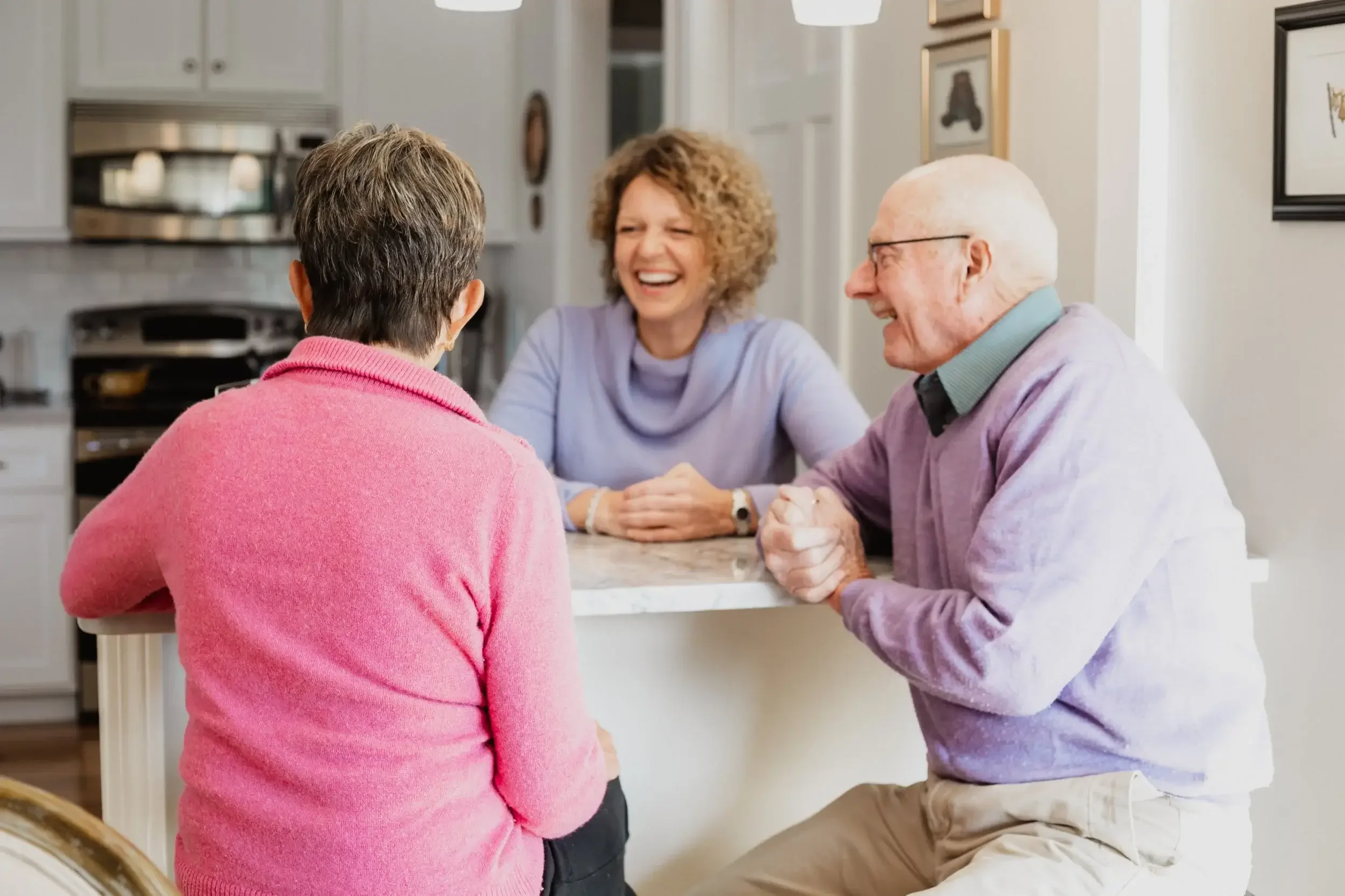 A couple and an older man and woman are seated together at a kitchen table, engaged in conversation.