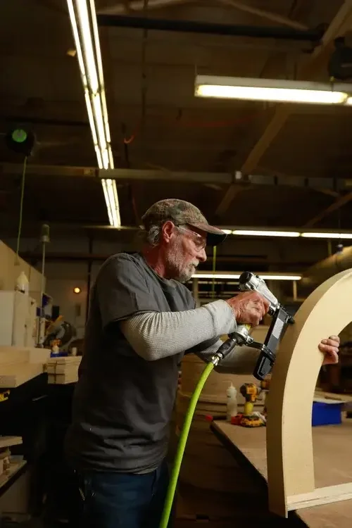  A man constructs a wooden arch in a workshop, surrounded by tools and wood materials.