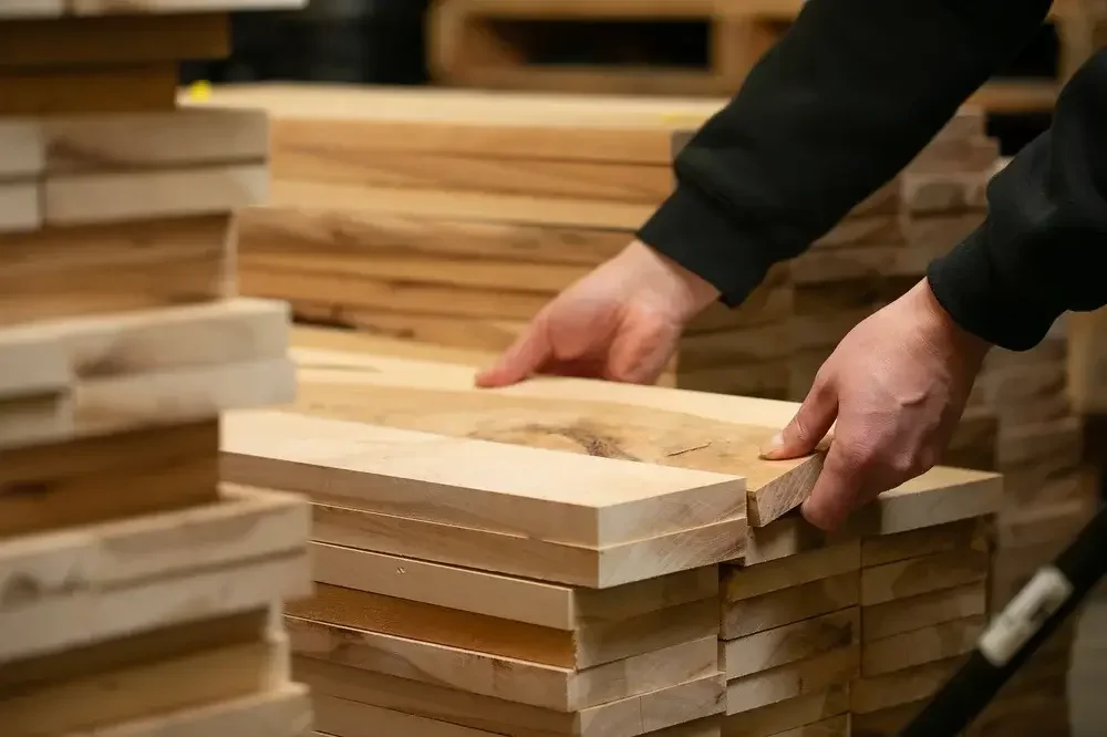 A man focuses on shaping a wooden plank in a well-lit workshop, surrounded by tools and materials.
