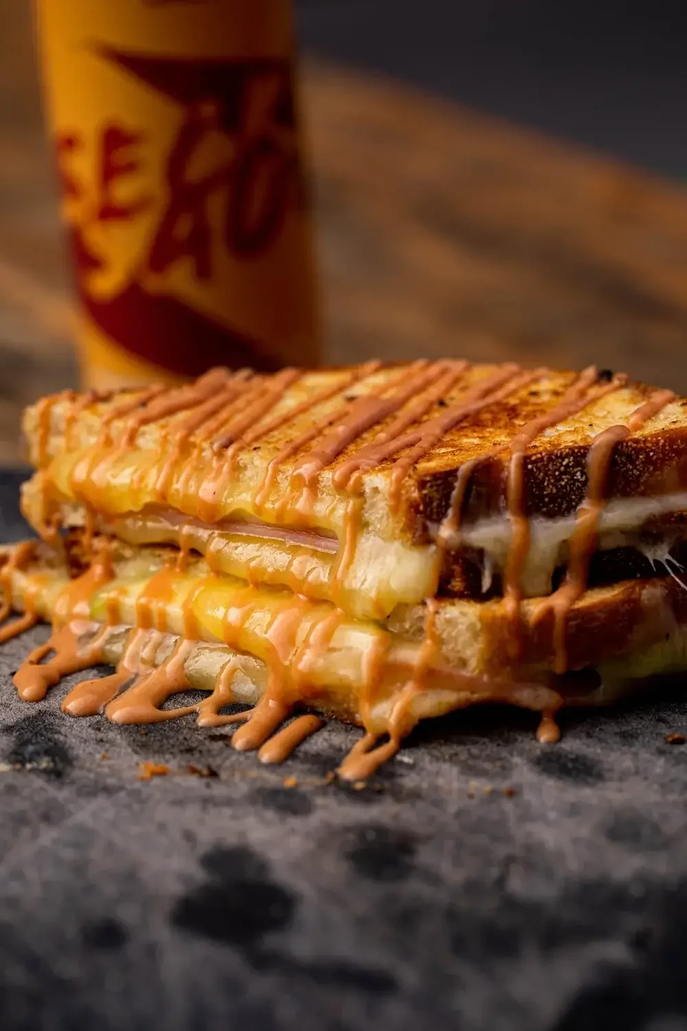 A grilled cheese sandwich drizzled with caramel sauce, accompanied by a can of Coke on a wooden table.
