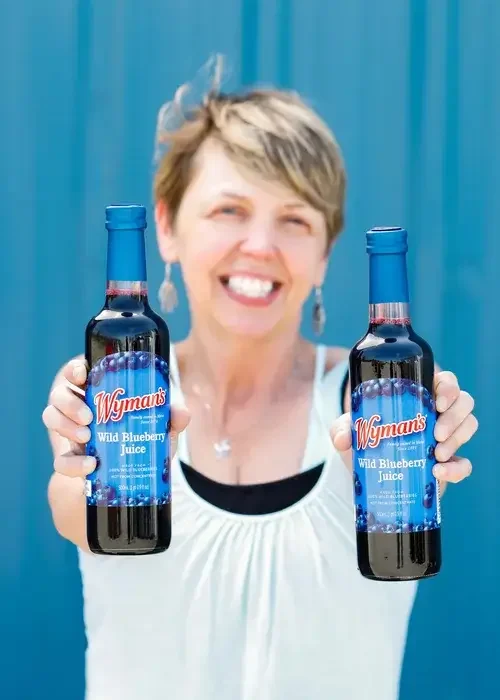 A woman holds two bottles of blueberry syrup, showcasing their labels and vibrant colors.