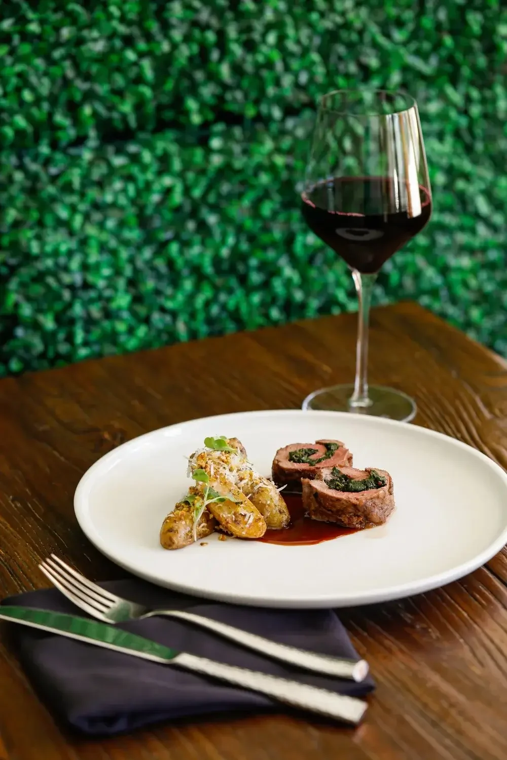  A plate featuring a serving of meat and potatoes alongside a glass of red wine.
