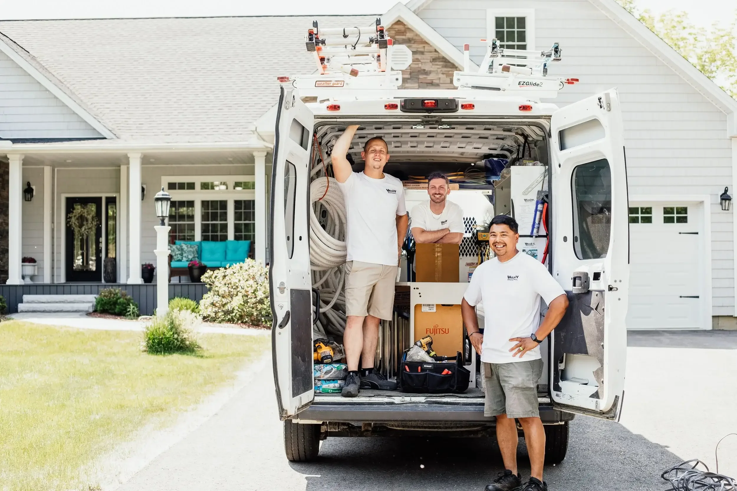 Three men stand together in front of a moving van, discussing logistics for their upcoming move.
