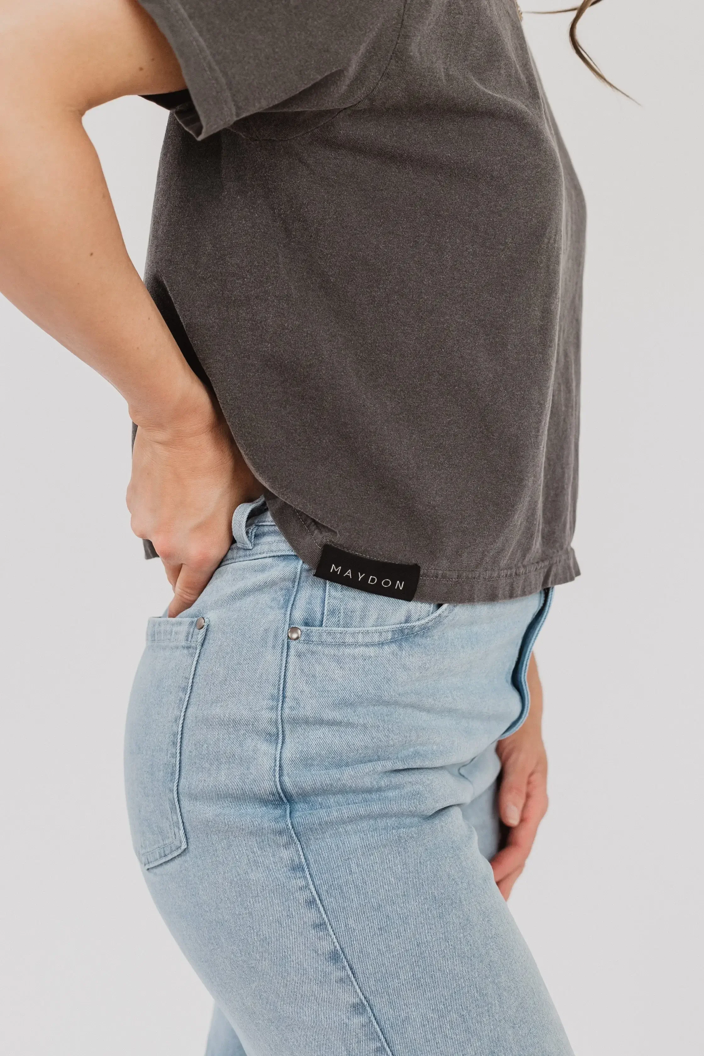 A woman seen from the back, wearing jeans and a gray t-shirt, standing in a casual pose.