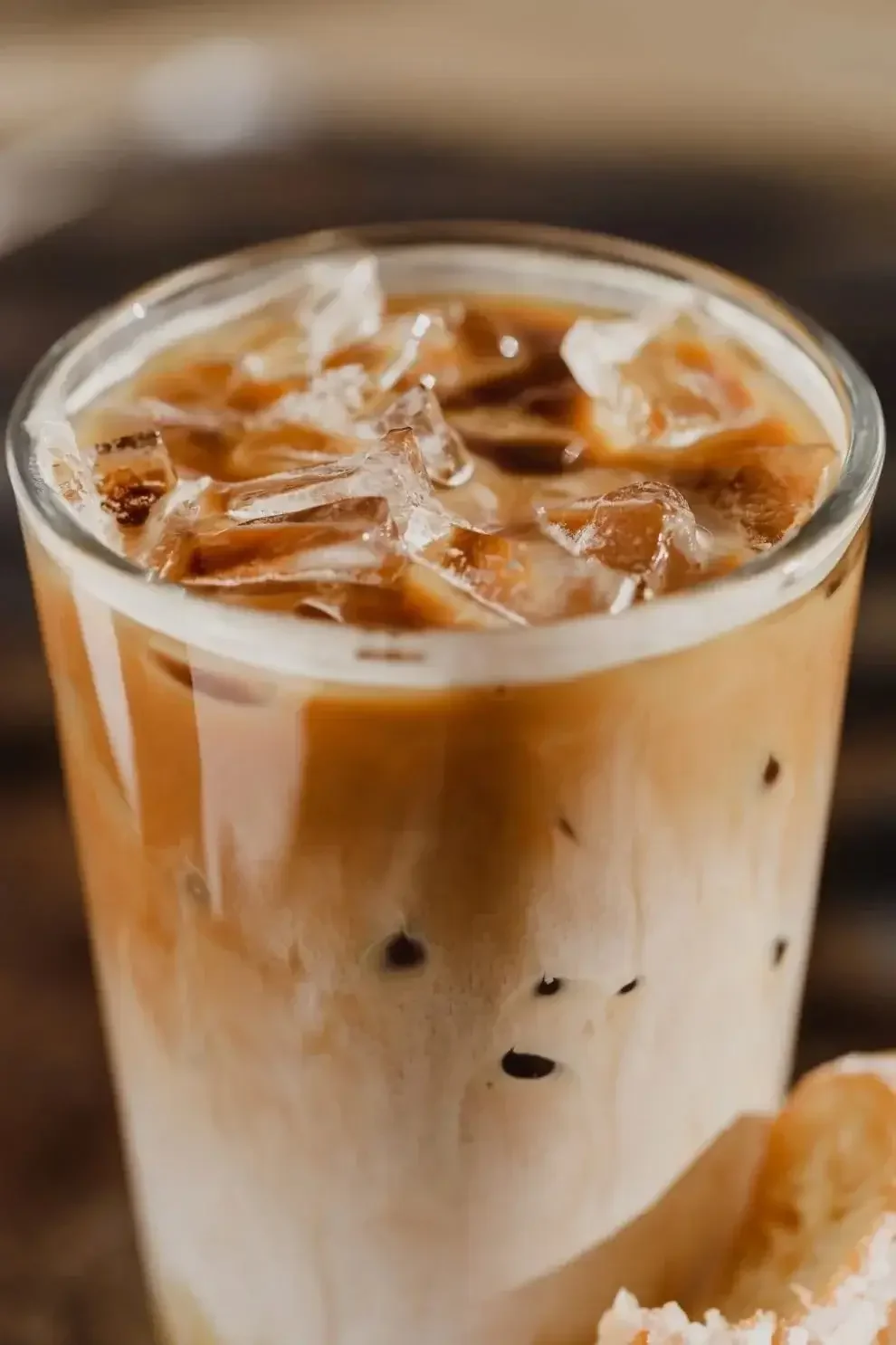  Iced coffee in a glass with ice cubes, accompanied by a ripe banana on a wooden surface.
