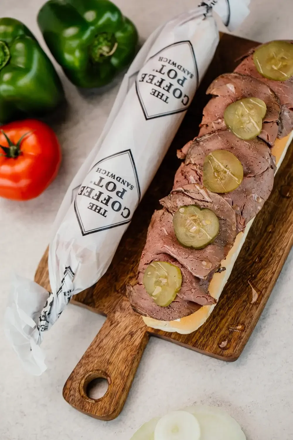 A sandwich with layers of meat and pickles displayed on a wooden cutting board.
