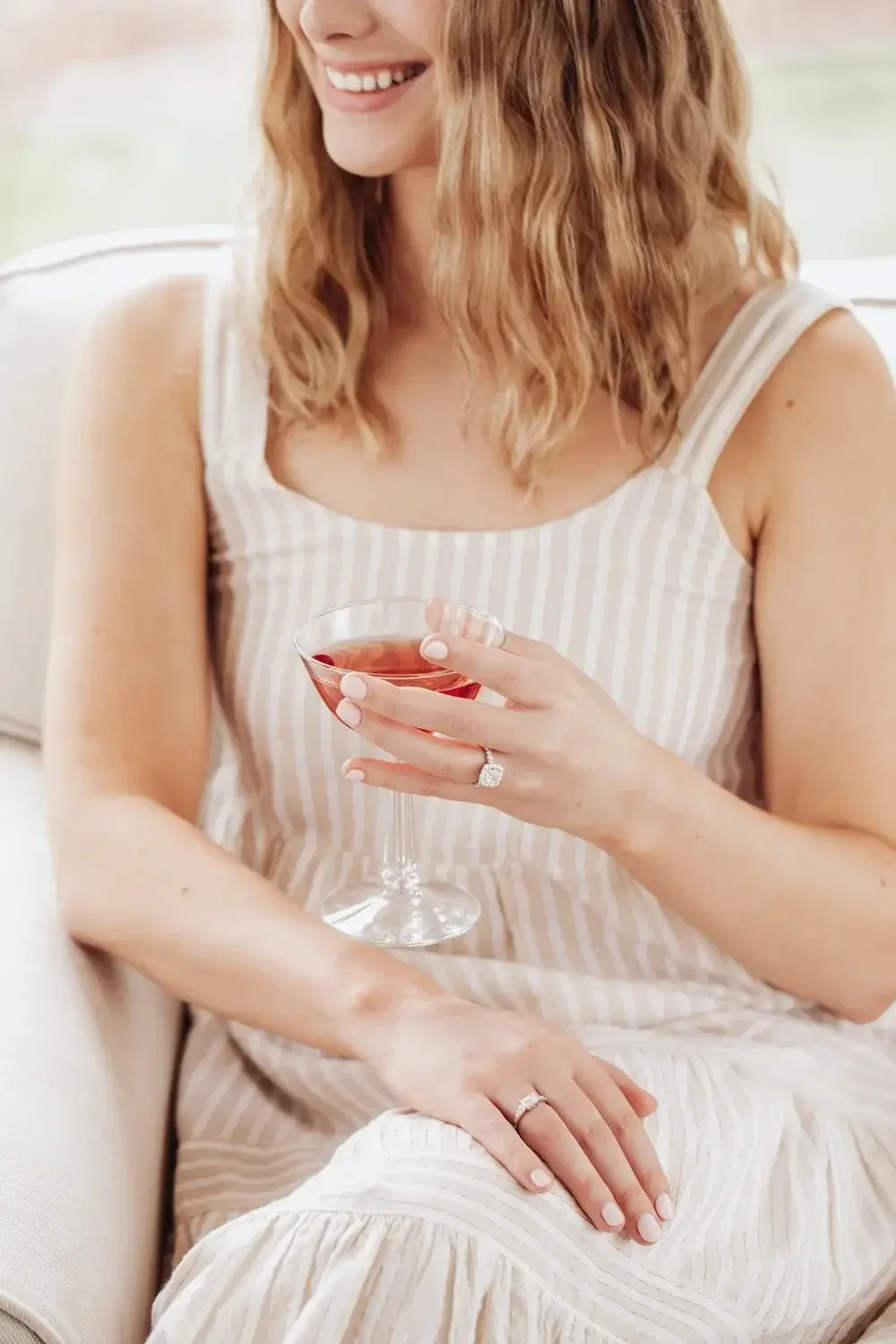 A woman sits on a couch, holding a glass of wine, with a relaxed expression on her face.
