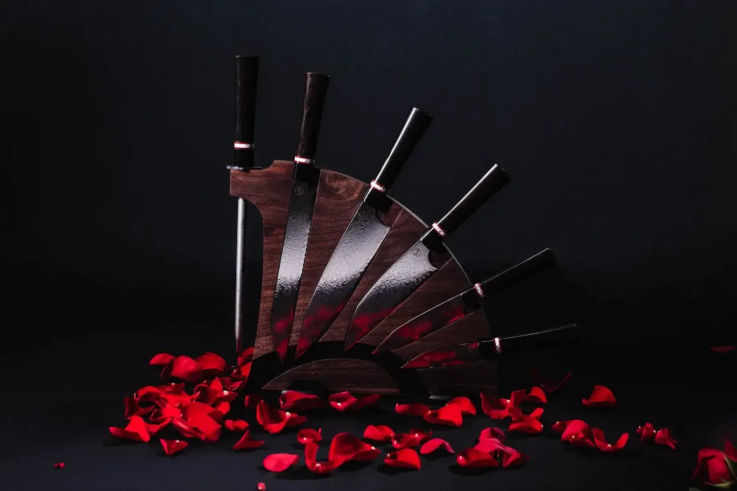 A set of kitchen knives arranged neatly, adorned with delicate rose petals on top for an elegant presentation.