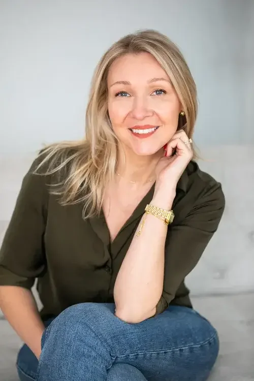 A woman sits on a couch, resting her chin on her hand, appearing thoughtful and contemplative.