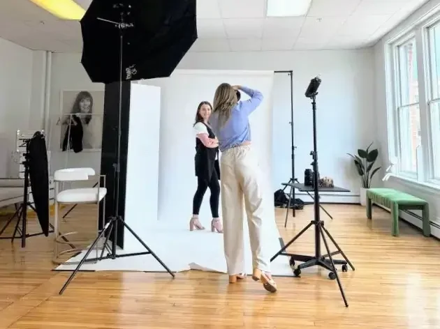 A woman stands in a studio, capturing a photo against a plain white backdrop.