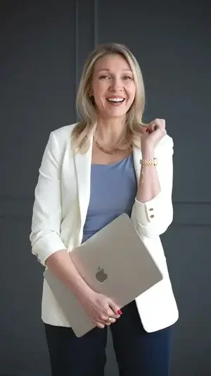 A professional woman wearing a white blazer holds a laptop, symbolizing readiness for a business meeting or presentation.