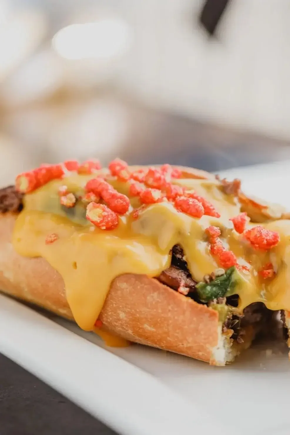A hot dog topped with melted cheese and a rich red sauce, served on a bun.
