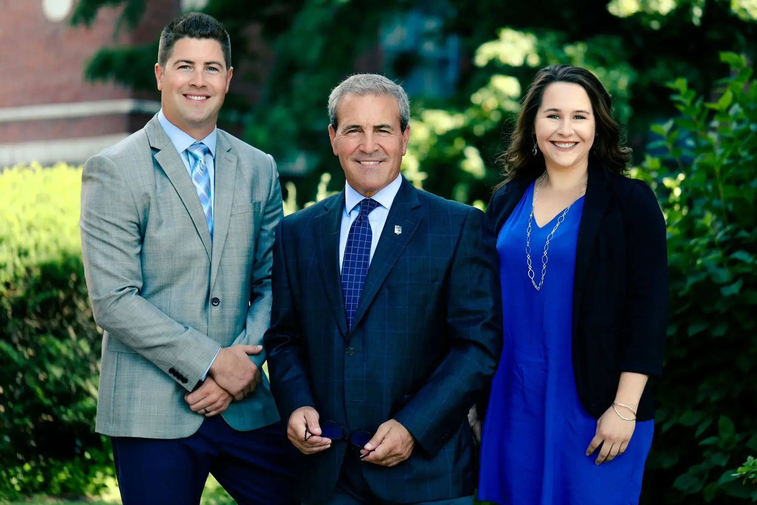 Three professionals in business attire pose together in front of a modern office building.
