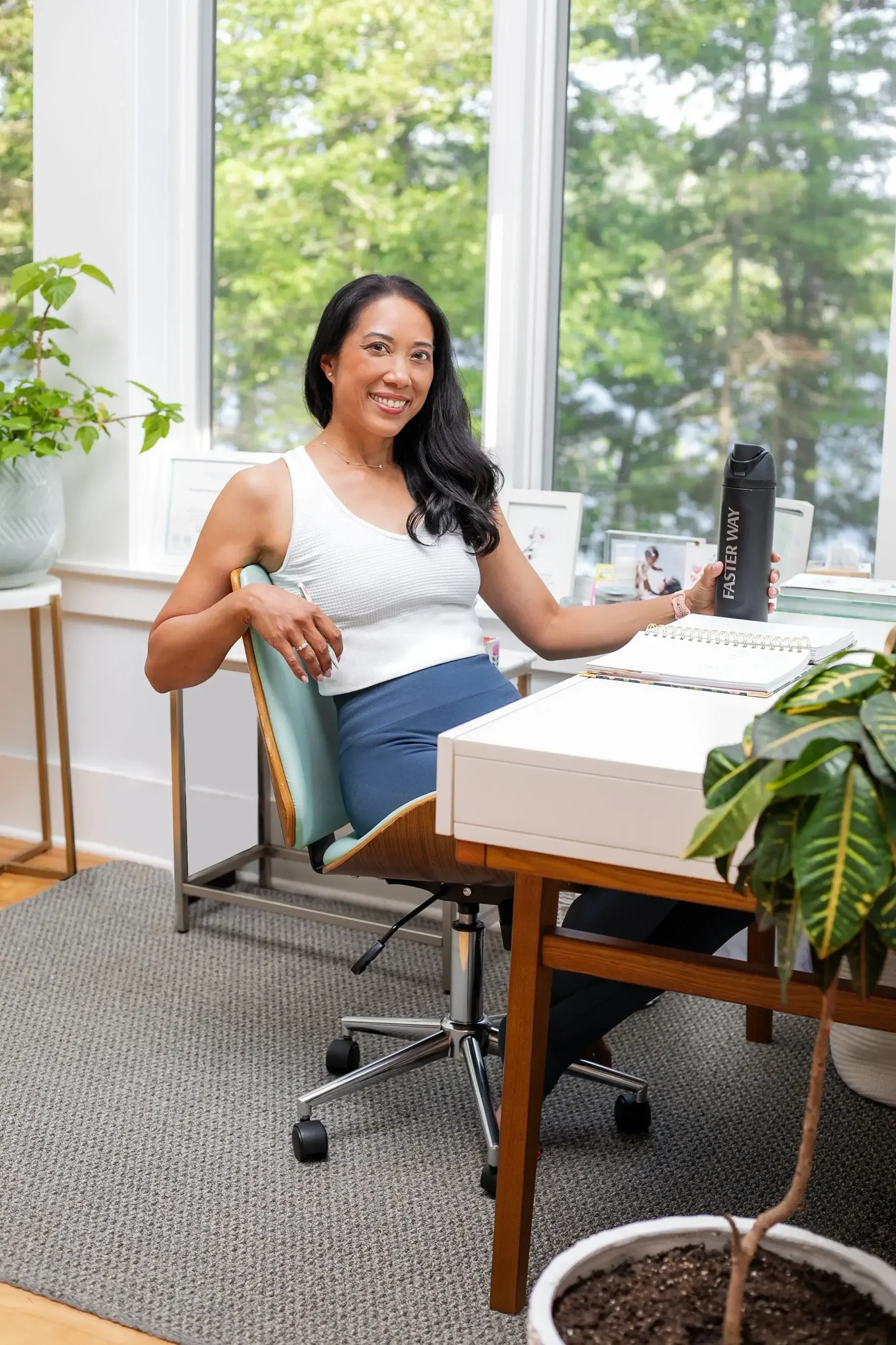 A woman seated at a desk, working on a laptop, with a small potted plant beside her.