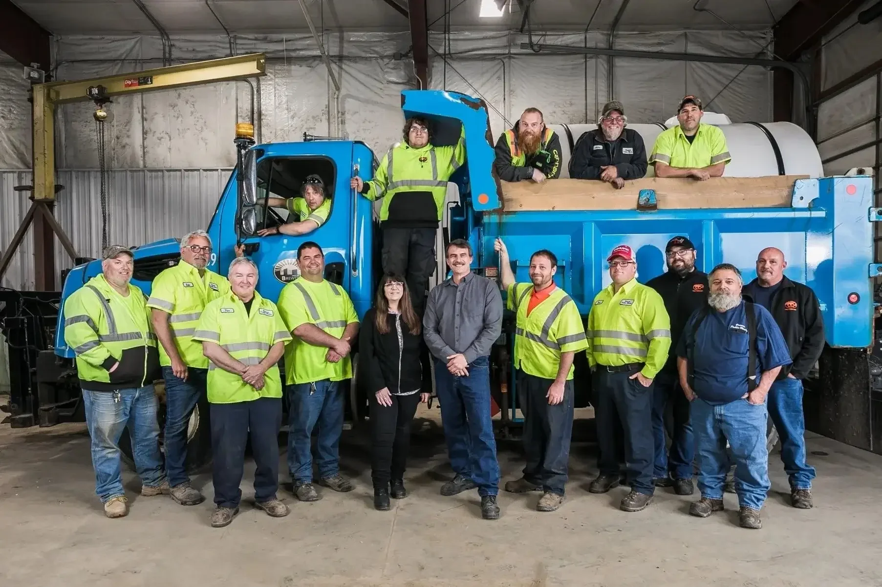A group of individuals in yellow vests stands beside a large truck, engaged in discussion or planning.