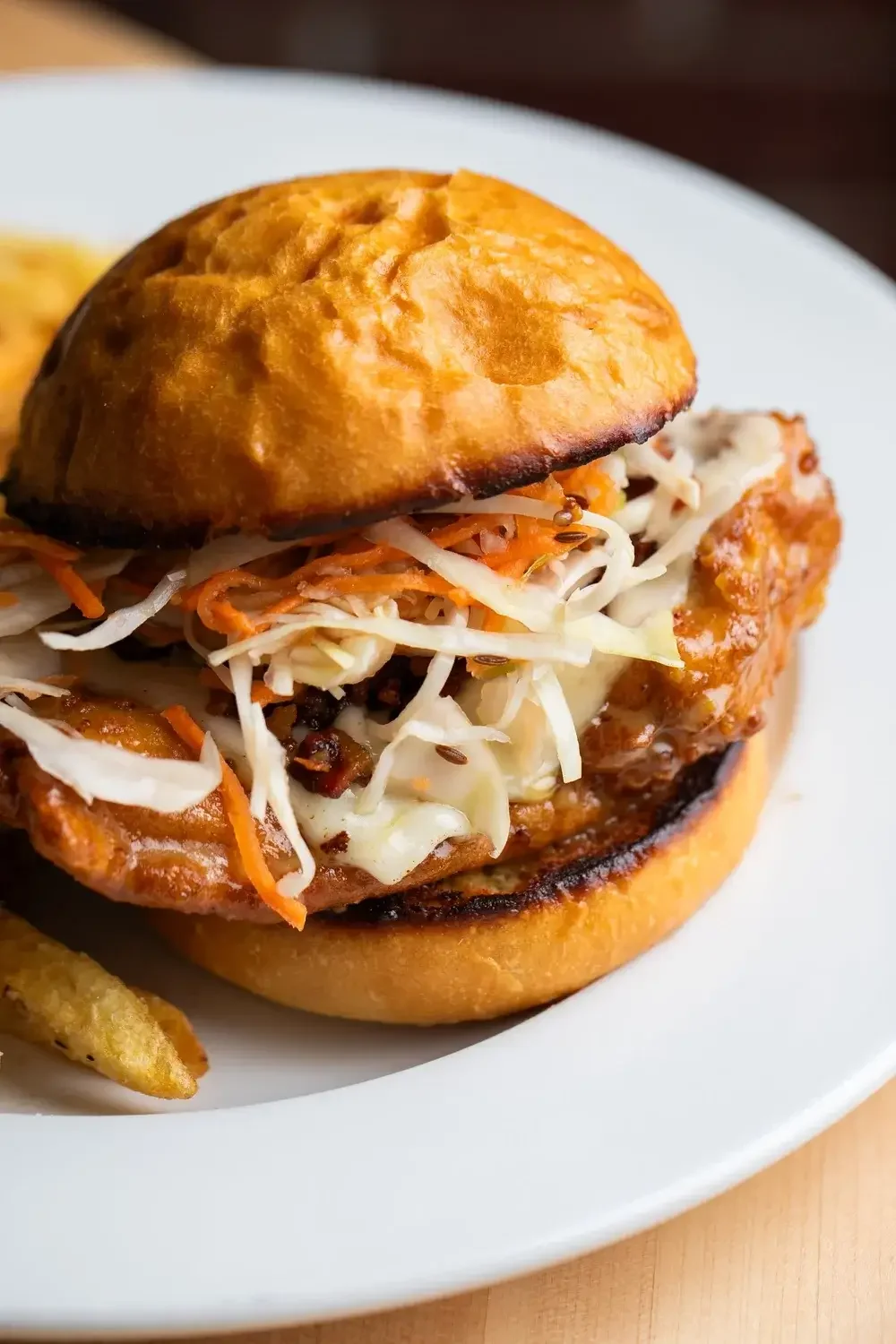 A chicken sandwich topped with slaw, accompanied by a side of chips, served on a white plate.
