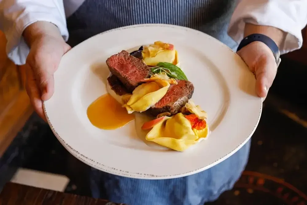 A chef proudly presents a plate of gourmet food, showcasing culinary skills and artistry.
