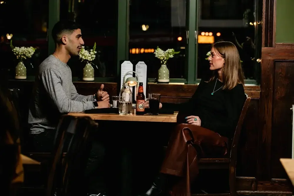 A man and woman seated at a restaurant table, engaged in conversation over a meal.
