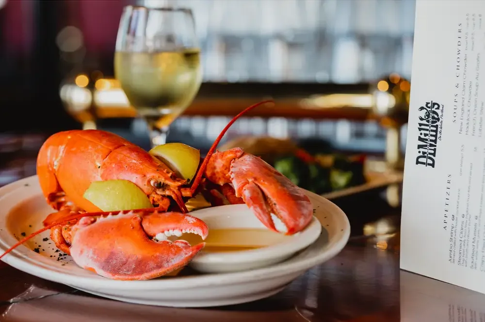  A cooked lobster on a white plate beside a glass of red wine, set on a wooden table.
