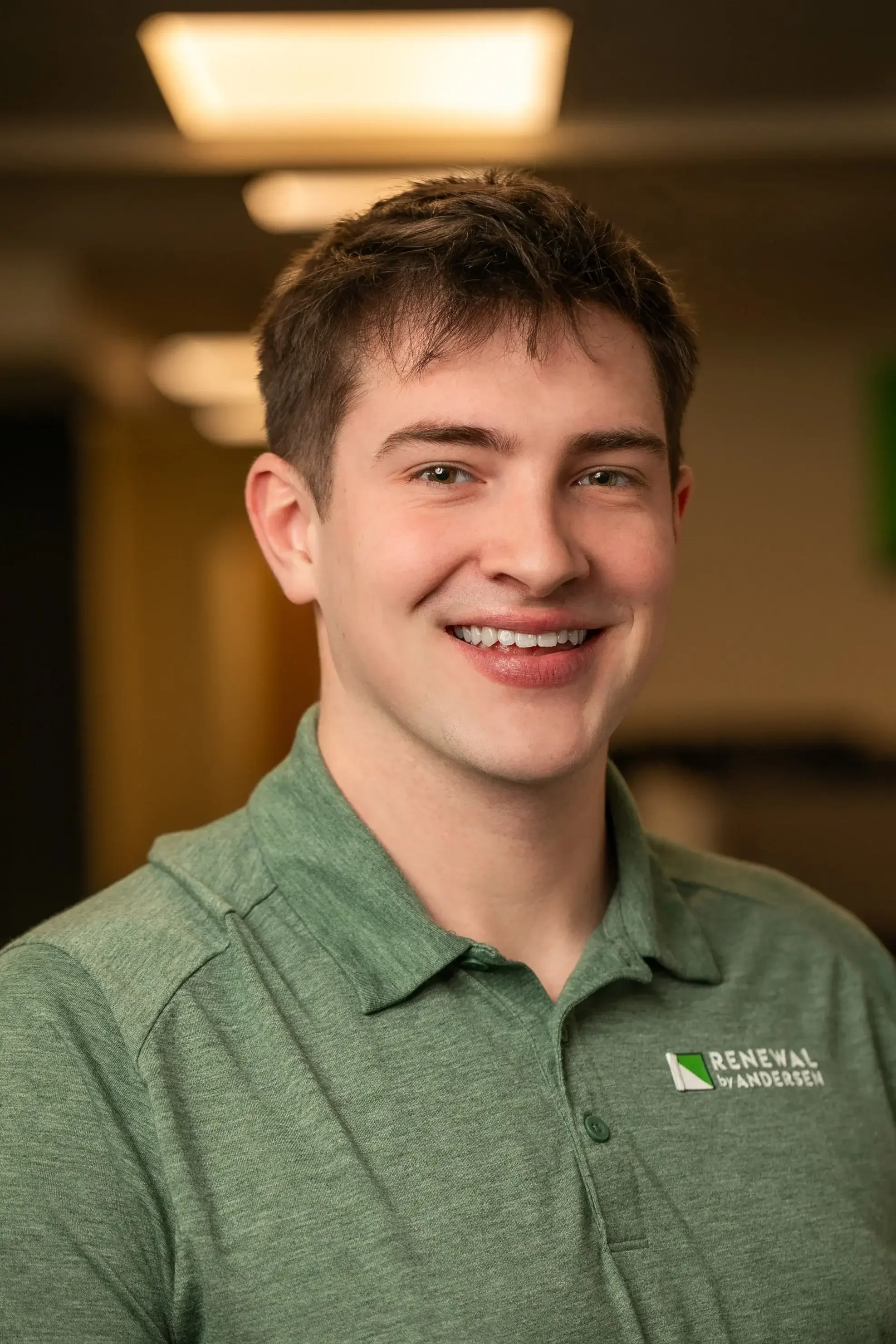 A young man wearing a green polo shirt smiles warmly at the camera.