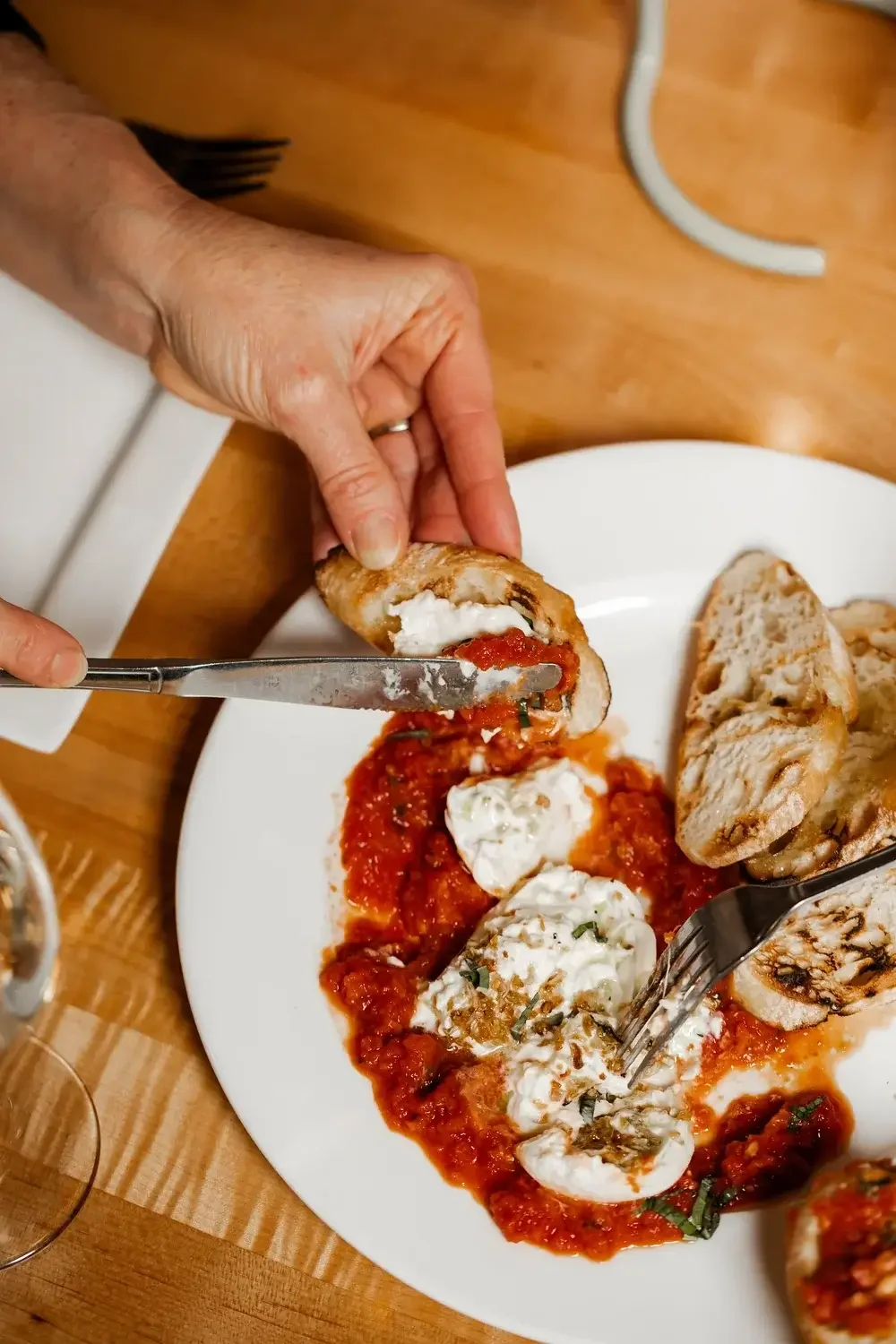 A person holds a knife and fork above a plate filled with a colorful meal, ready to eat