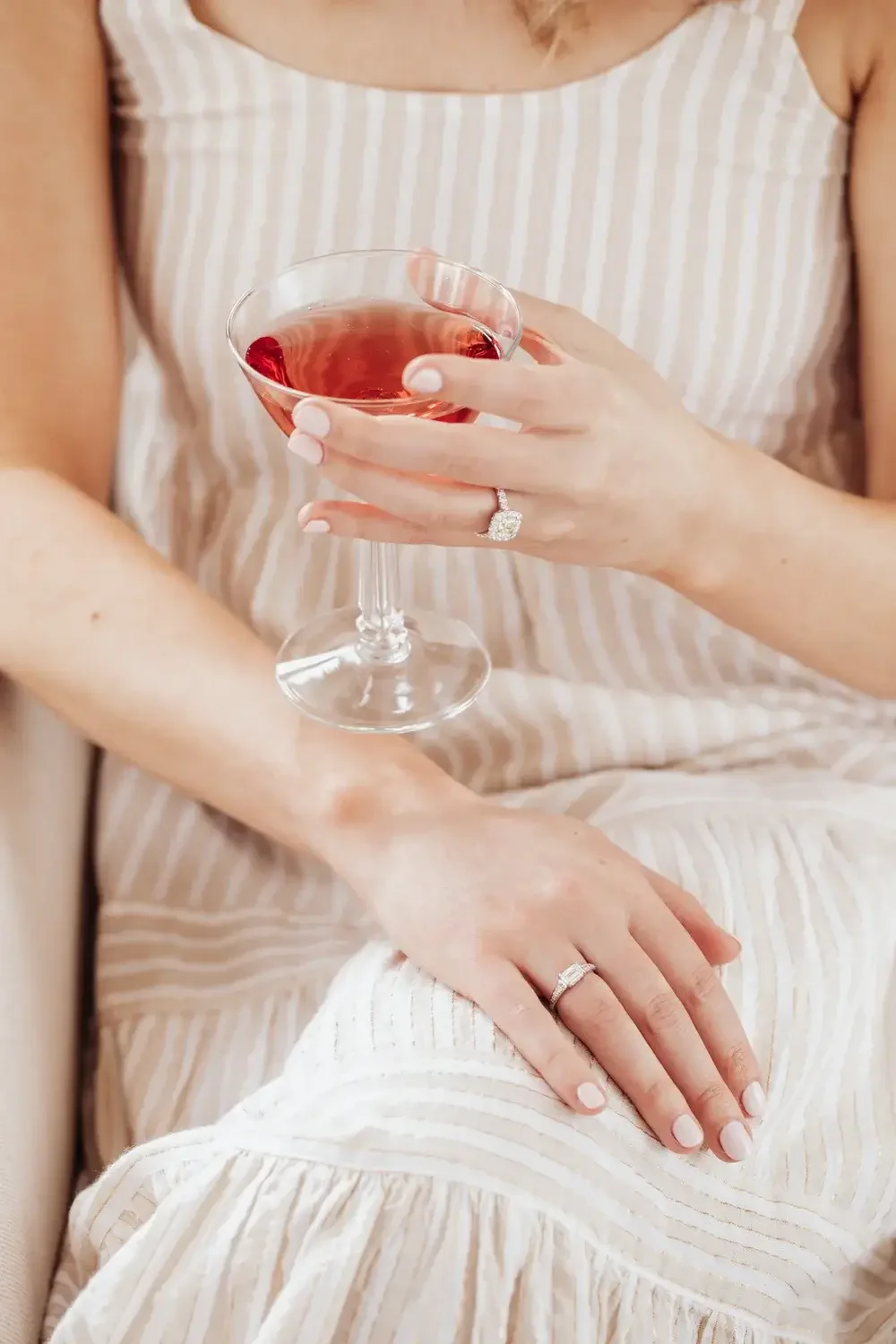  A woman elegantly holds a glass of wine, showcasing her wedding ring on her finger.