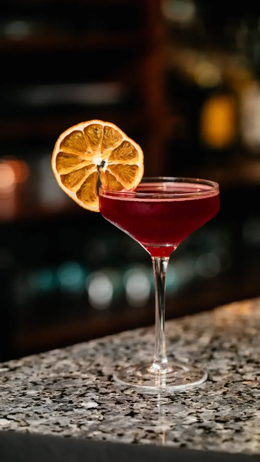 A vibrant red cocktail garnished with a fresh orange slice on the rim of the glass.