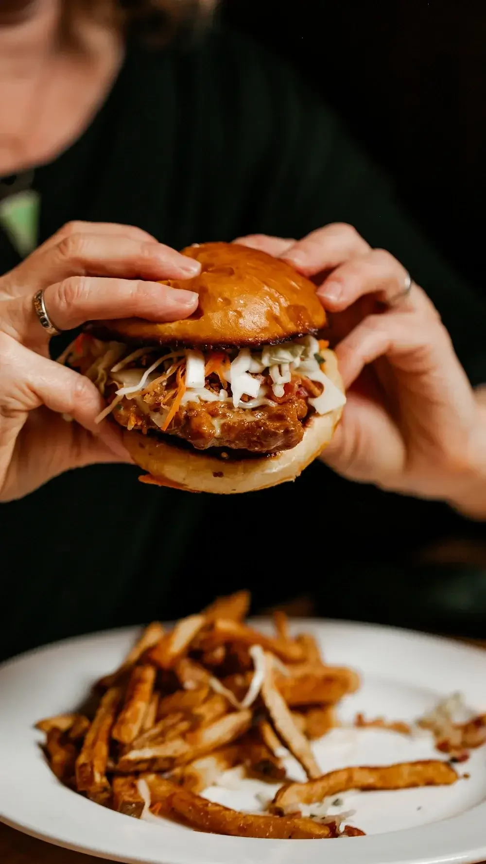 A person holding a juicy burger with a sesame seed bun and a thick beef patty, ready to take a bite.