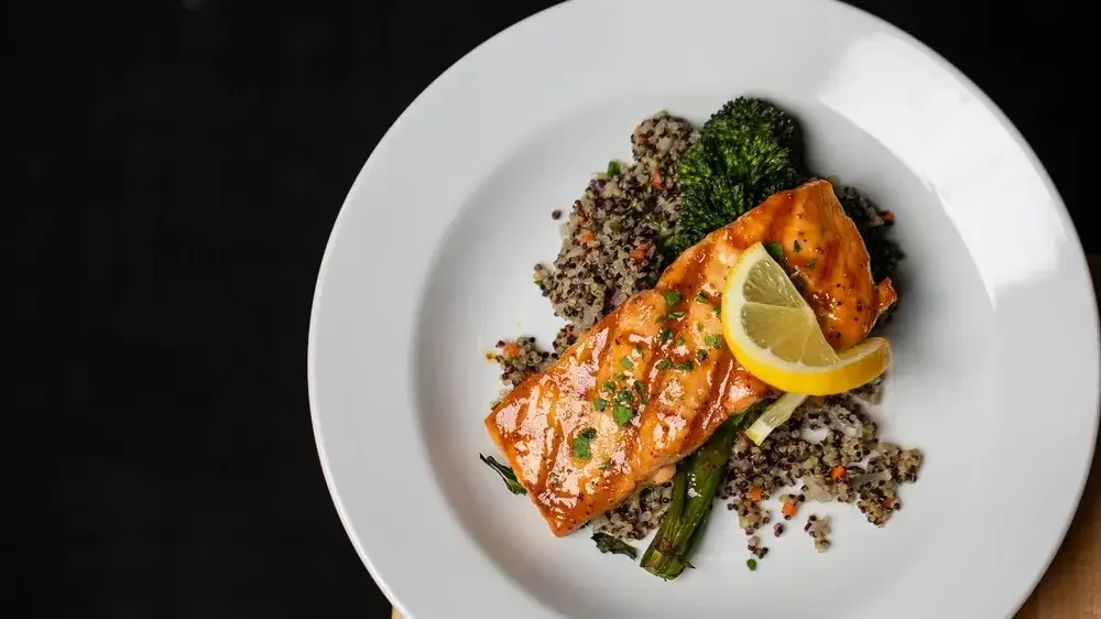 A plate featuring grilled salmon, steamed broccoli, and a fresh lemon wedge for garnish.
