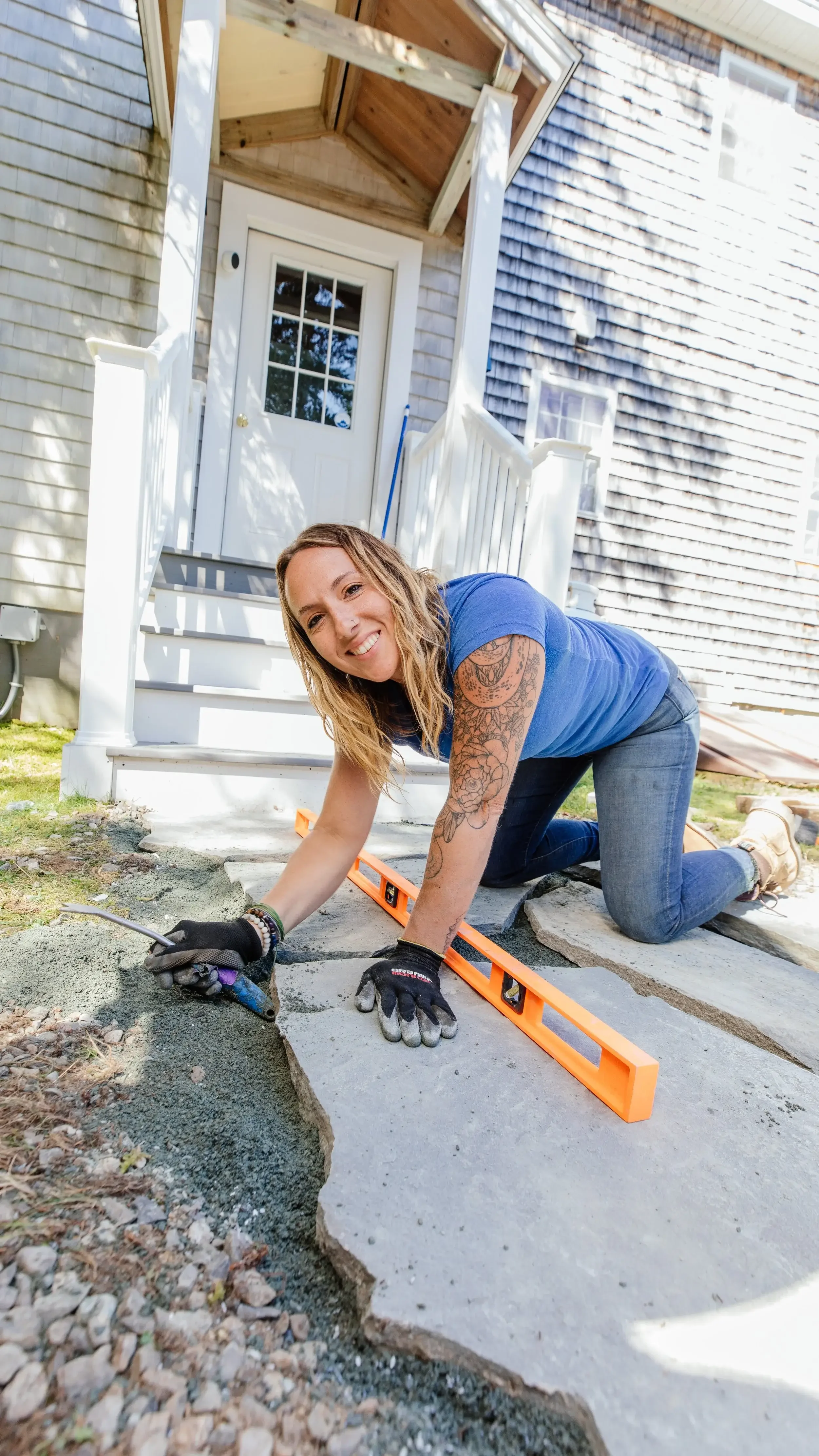 A woman lies on the ground, holding a tool, focused on her task in an outdoor setting.