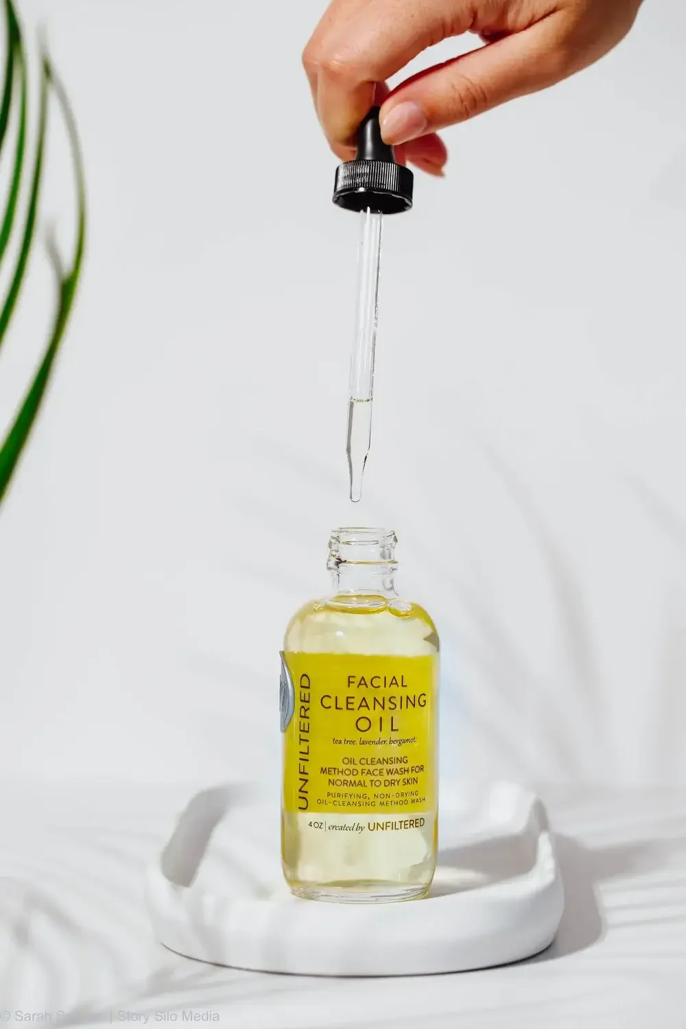  A bottle of facial cleansing oil placed on a white plate, showcasing its sleek design against a neutral background.