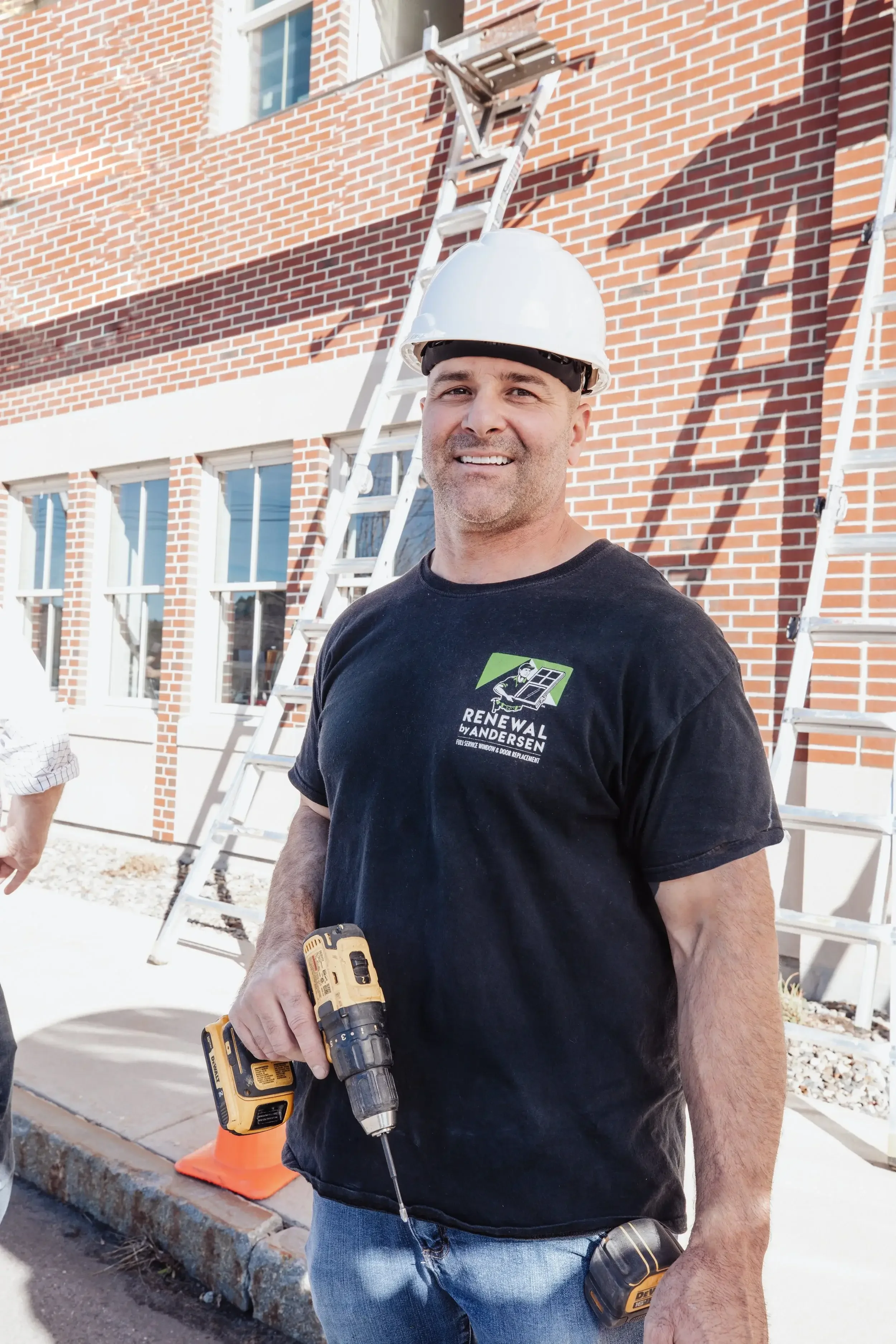 A man wearing a hard hat and black shirt is holding a drill, ready to work on a construction project.