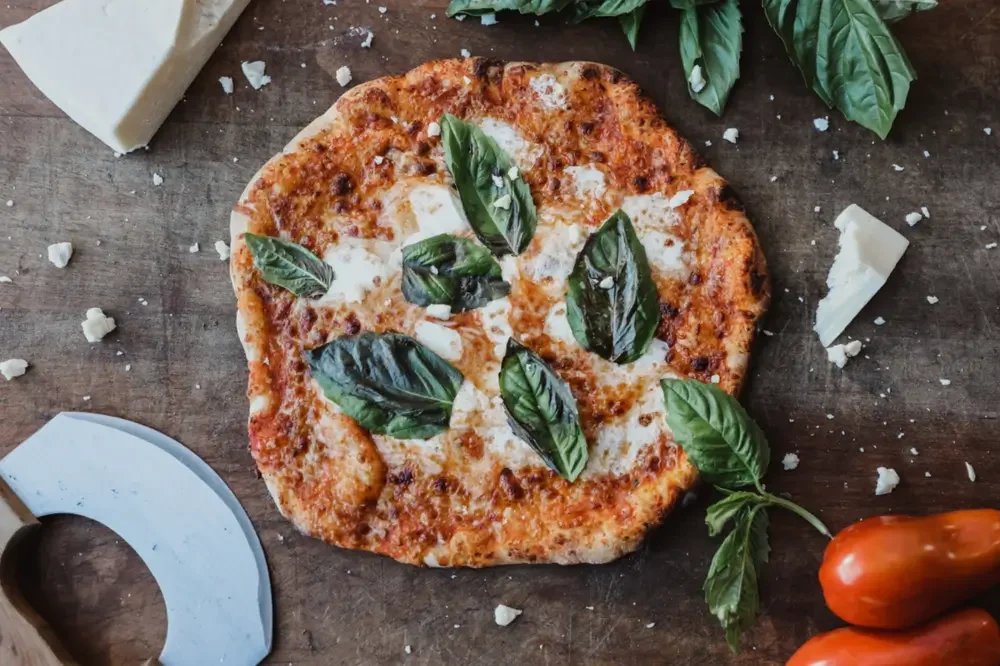A freshly made pizza topped with basil and cheese, resting on a wooden cutting board.