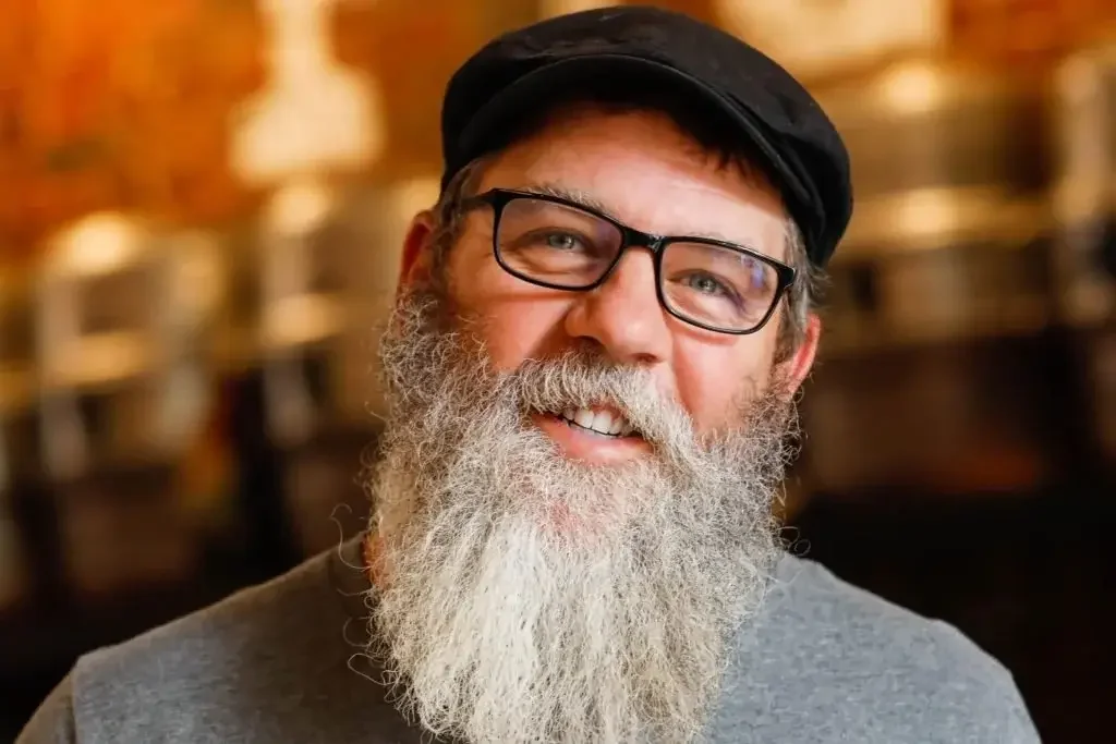 A smiling man with a beard and glasses, exuding a friendly and approachable demeanor