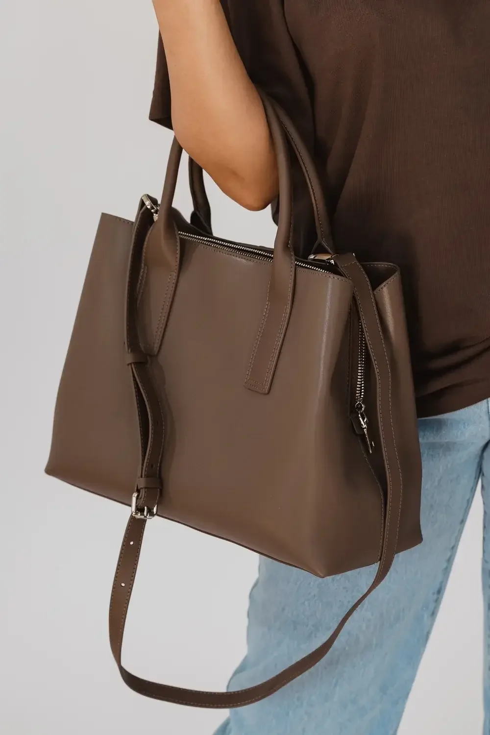 A brown leather tote bag displayed against a neutral background, showcasing its sleek design and sturdy handles.