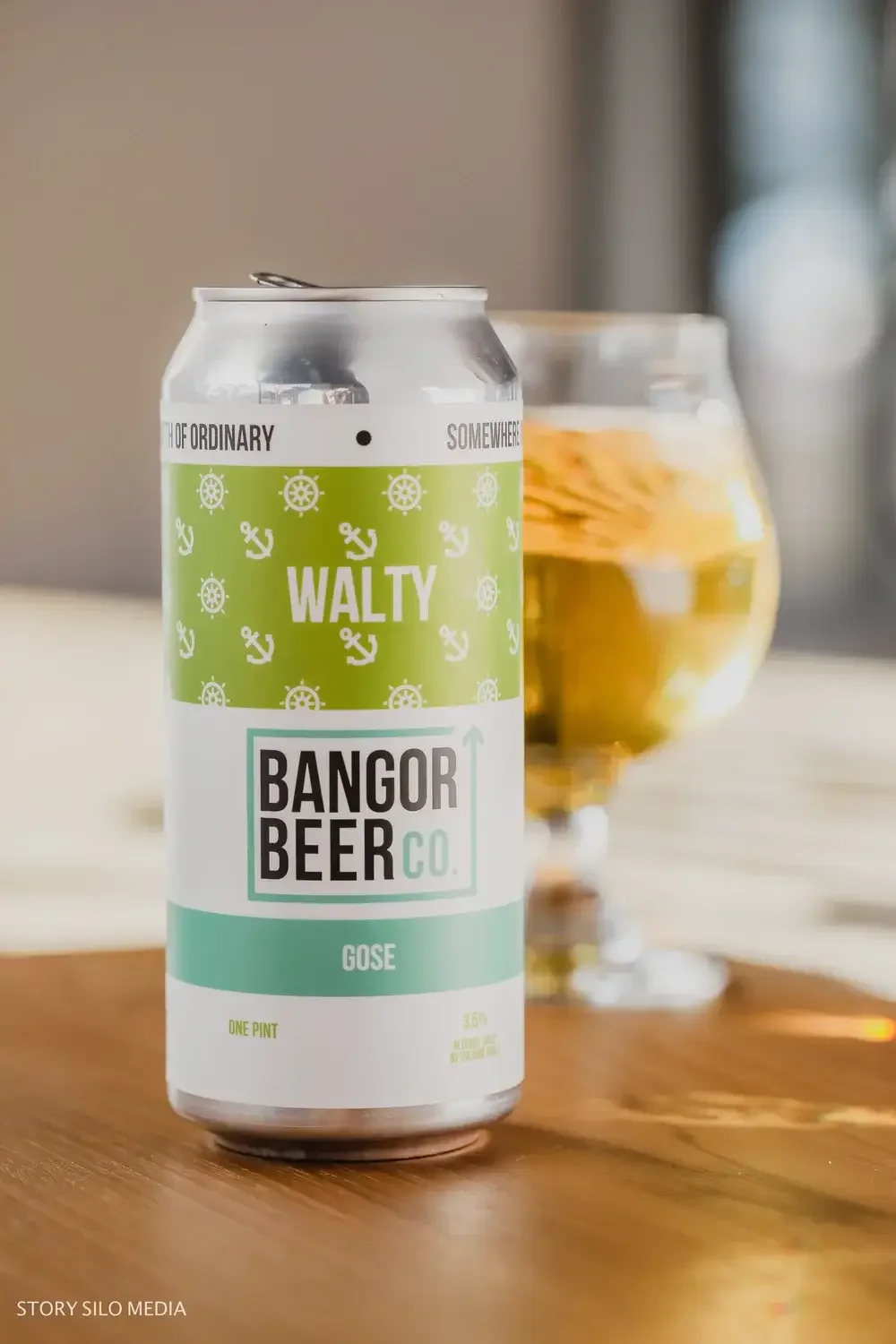 A can of beer placed beside a filled glass of beer on a wooden surface.

