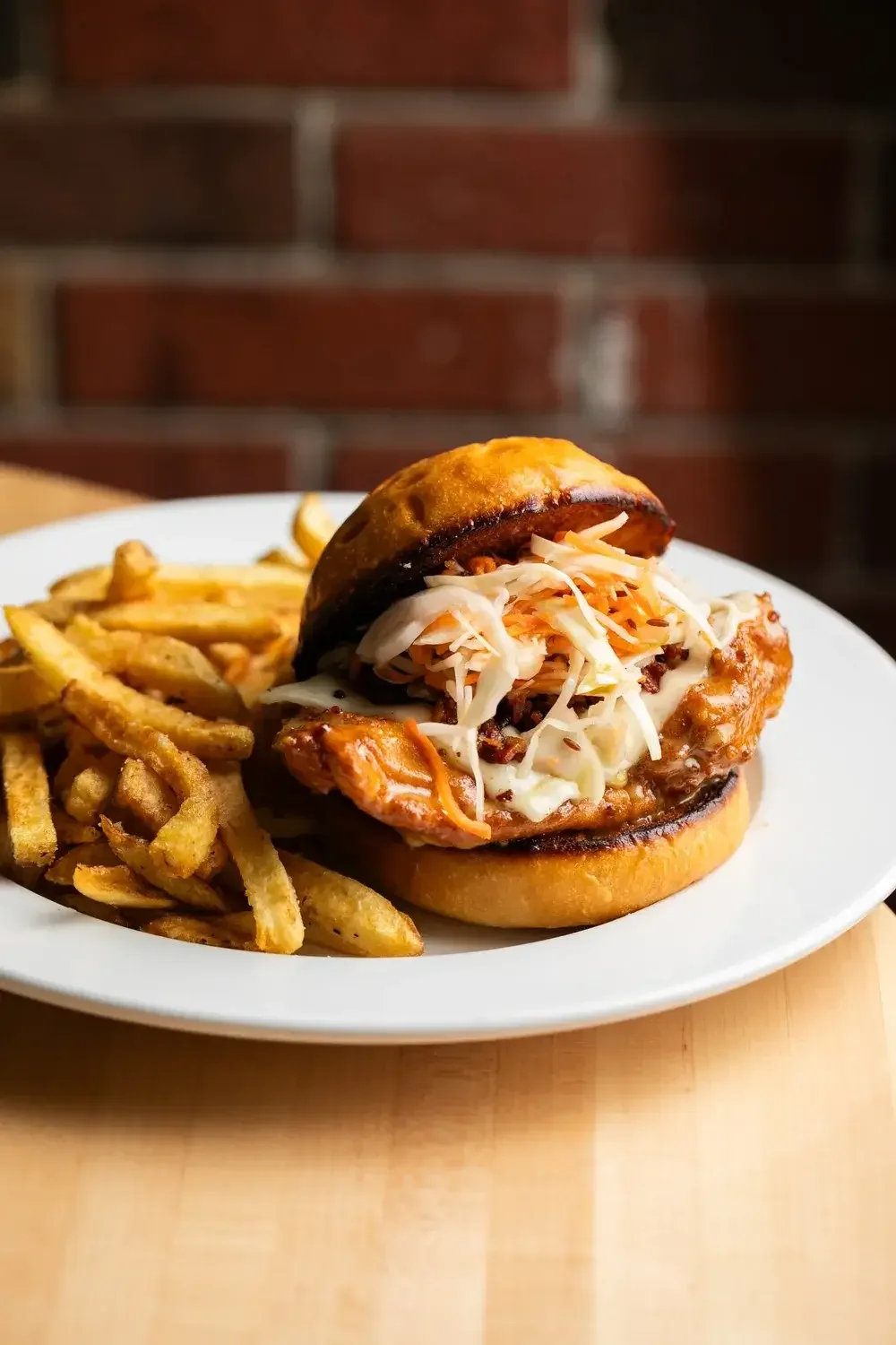 A chicken sandwich topped with coleslaw, served alongside a portion of crispy French fries.