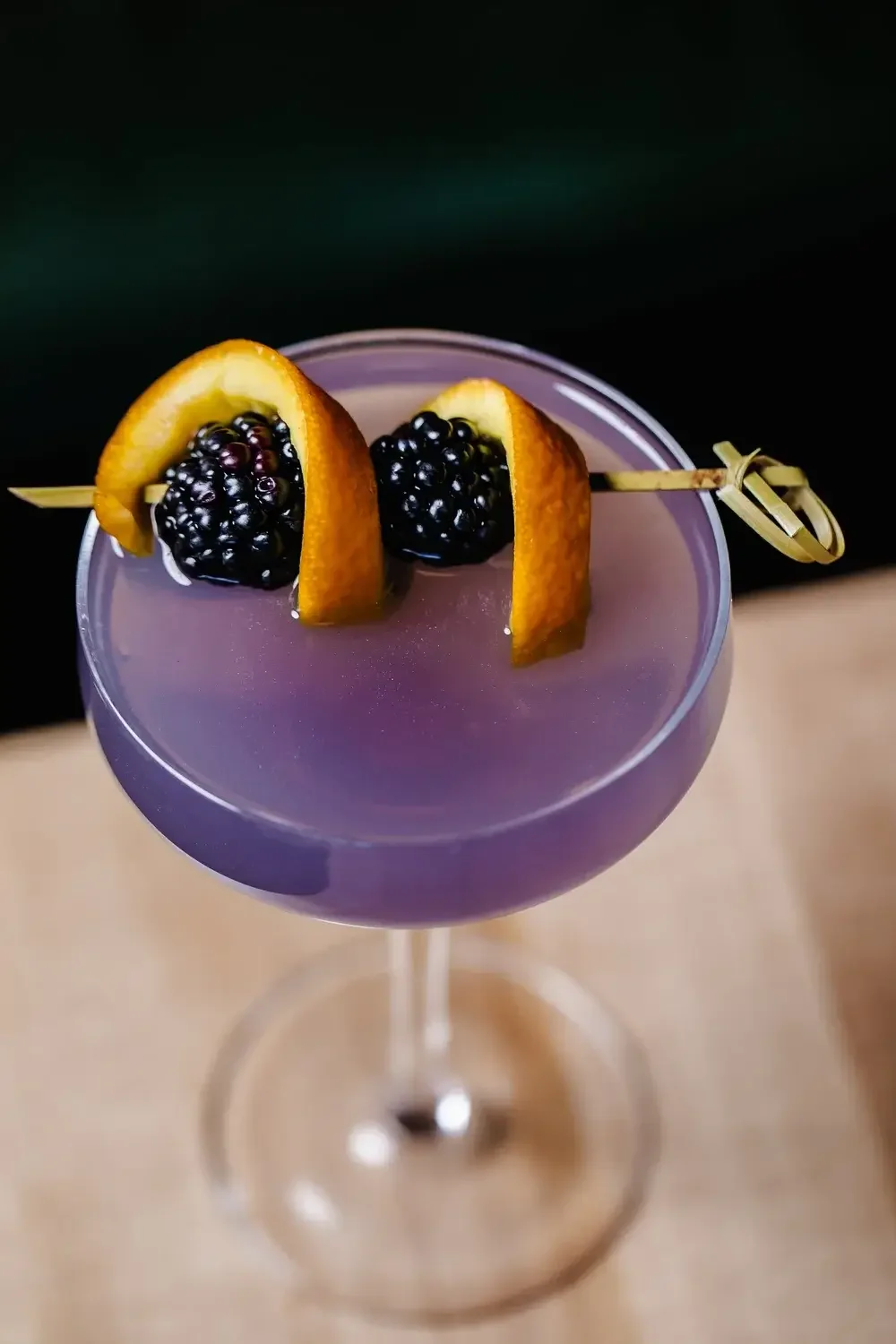 1. A vibrant purple cocktail garnished with fresh blackberries and orange slices, served in a clear glass.
