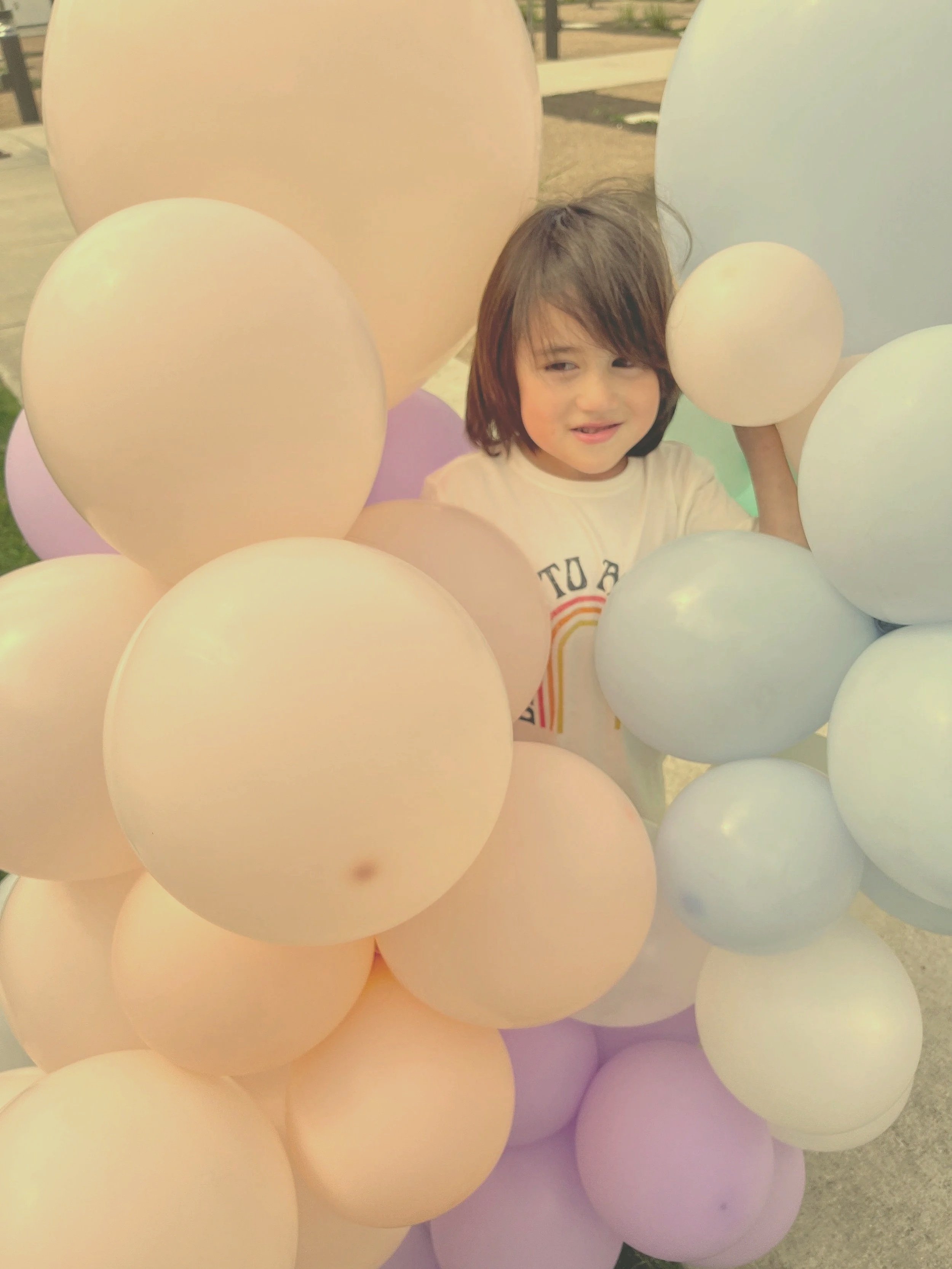 Child surrounded by colorful balloons outdoors