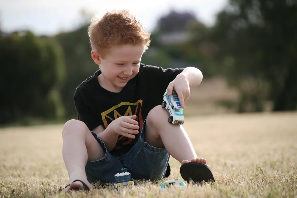 Child playing with toy cars on grass in a park.