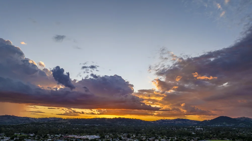 Sunset with dramatic clouds over a cityscape and hills.