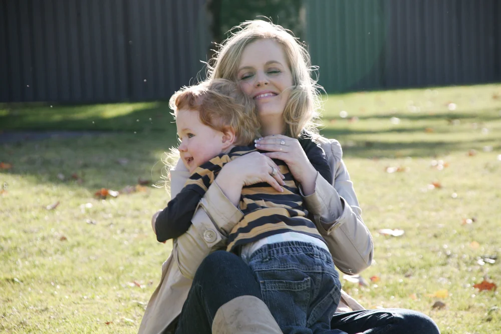 A woman hugging a small child on grassy field
