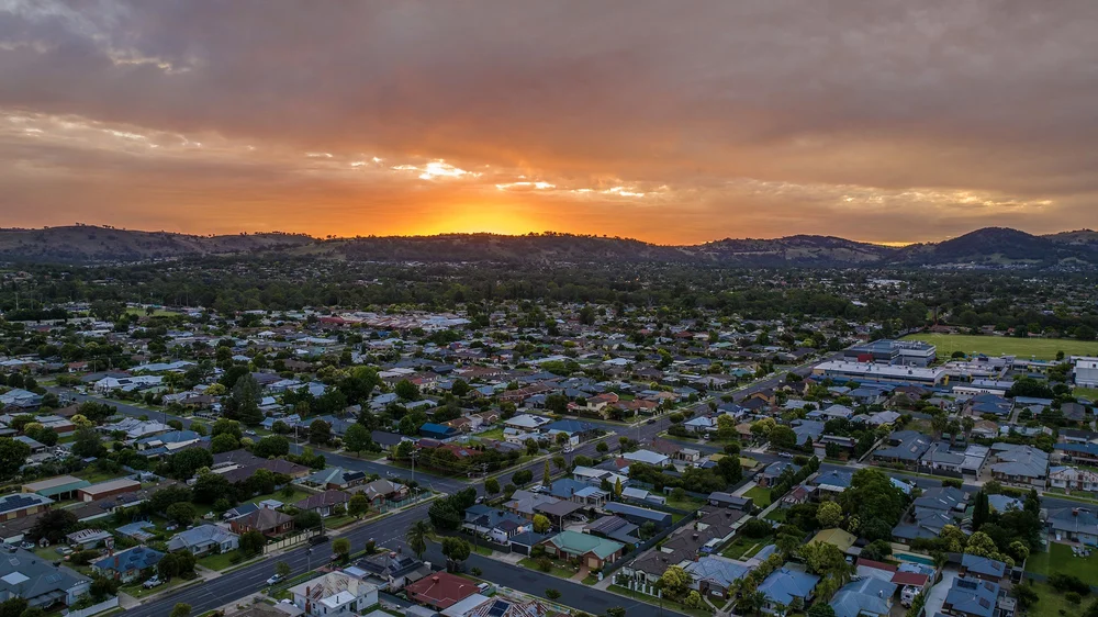 Aerial view of a suburban residential area at sunset with hills in the background.